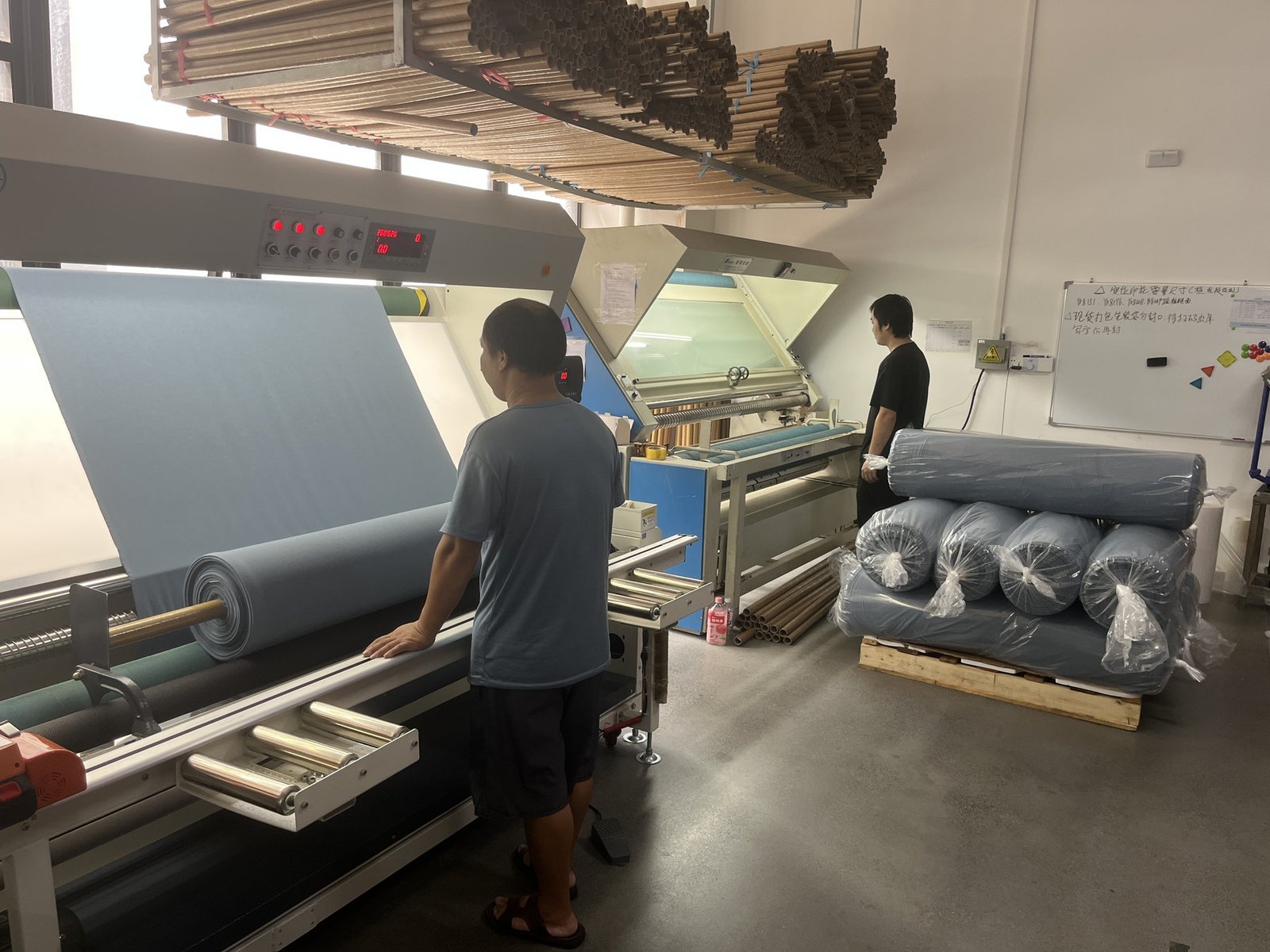 Workers inspecting finished fabric at a rolling machine
